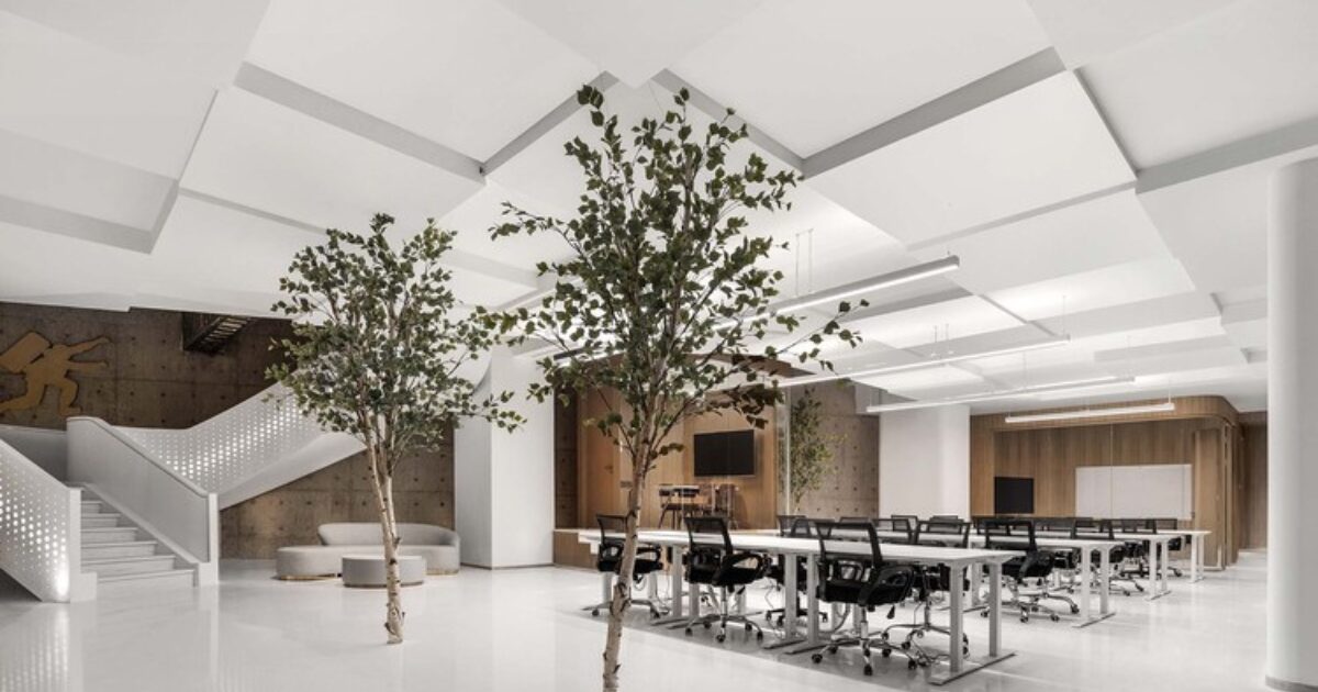 白を基調とした広いオフィス空間に、観葉樹が配置され、長テーブルとオフィスチェアが整然と並んでいる様子